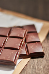 dark chocolate in paper packaging on a wooden table.