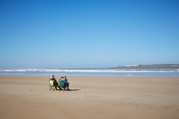 Fototapeta na wymiar Ein Paar sitzt am leeren Strand und schaut mit dem Fernglas 