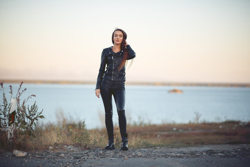 beautiful sexy girl with long hair in a leather jacket and leather pants standing on the beach at...