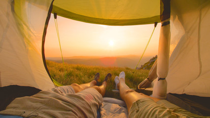 SUN FLARE: Young couple moving their feet as they watch the sunset from the tent © helivideo