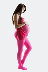 Pregnant woman in pink leggens tender holding her belly at the white background,  isolated