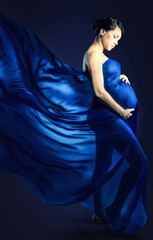 Portrait of a pretty young woman holding pregnant belly in  fluttering fabric, naked