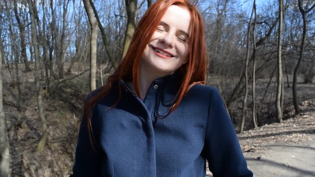 Portrait of a red-haired girl on the background of dry branches in the Park.