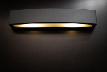 Black metal angular wall lamp with yellow light on with copy space