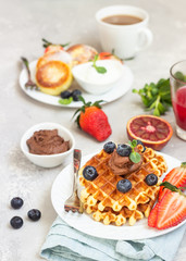 Belgian waffles with chocolate sauce, berries and mint and cottage cheese pancakes on a light gray background. Breakfast or lunch. Copy space.