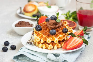 Belgian waffles with chocolate sauce, berries and mint and cottage cheese pancakes on a light gray background. Breakfast or lunch. Copy space.