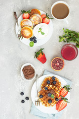 Belgian waffles with chocolate sauce, berries and mint and cottage cheese pancakes on a light gray background. Breakfast or lunch. Copy space.