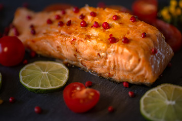 Fried sea fish and a tomato. A salmon decorated by spices of pink peppercorn. Food. Blurry background. Soft focus. Closeup.