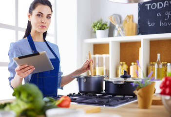 Young woman using a tablet computer to cook in her kitchen