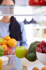 Smiling woman taking a fresh fruit out of the fridge, healthy food concept