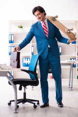 Young handsome businessman with longboard in the office