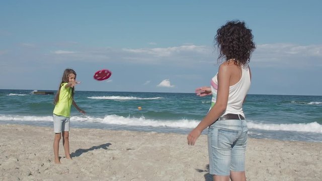 Family playing with flying disc on beach. Cheerful little girl with her mother play frisbee on an empty beach.