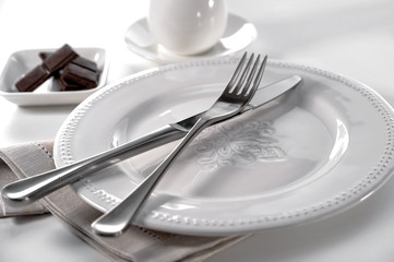 classic table setting cutlery knife and fork on porcelain plate, linen cloth, bowl of chocolate...