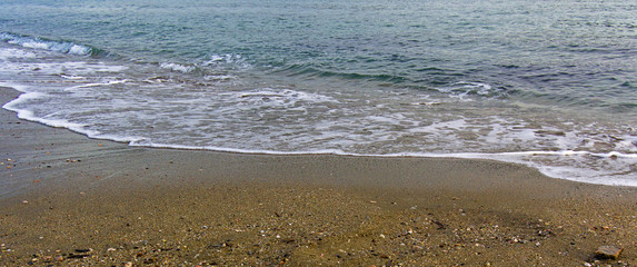 Sea wave reaching sandy beach. Colorful water and sand. Beautiful coast detail, panorama image.
