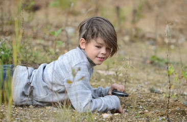 Naklejka na ściany i meble a boy in nature sitting on the ground looking at a magnifying glass plants