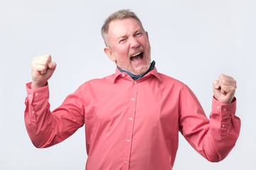 Senior man very glad to win, gesturing with fists.