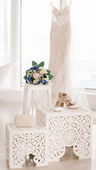 A wedding bouquet, bridal shoes and a pearl clutch stand (lie) against the background of a white wedding dress. Accessories for the bride.