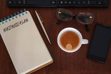 Top view of Office desk with office accessories and notebook with Business Plan written. Business plan strategy concept