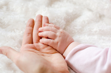 Little baby hand on mother's palm on white fluffy background