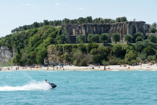 Stony Beach of Sirmione town on Garda Lake with view of Grottoes of Catullus (Grotte di Catullo), the ruins of a Roman villa built at the end of the 1st century B.C. View from Garda Lake.