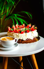 Coffee and brownie with whipped cream and fruits, cup of cappuccino on white table with green background.