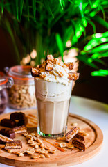 Coffee with whipped cream, sweets and peanuts on wooden table, green background.