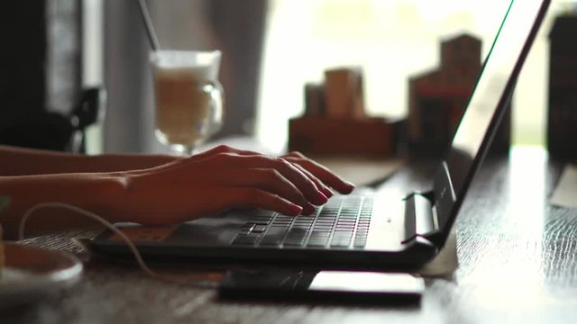 4k Female hands type on laptop keyboard touching touchpad with fingers smart phone lying near close up. No face woman sits on sofa freelancing working at home writes post comments in social networks
