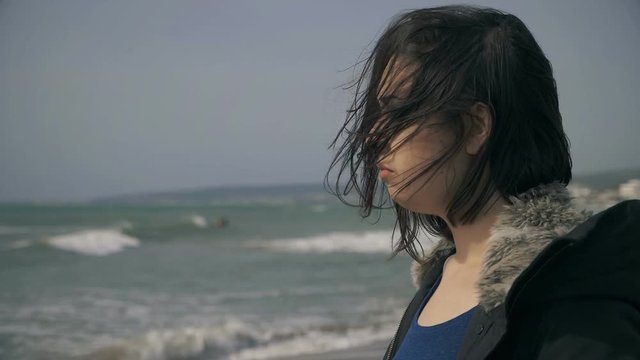 portrait of sad pensive Young beautiful woman standing alone on the beach in windy day