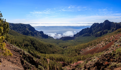 Landscape of mountains with a black volcanic caldera and clouds over the ocean in the background