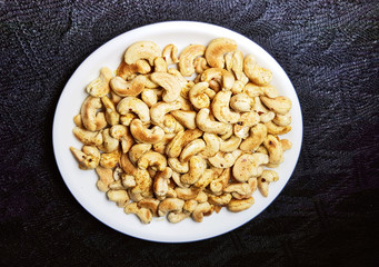 Fried and spiced cashew nuts in white plate on dark background