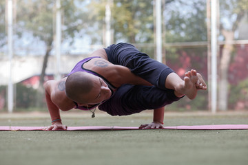 tattooed skinhead woman in Eight-Angle yoga Pose, Astavakrasana,  on green lawn in summer park