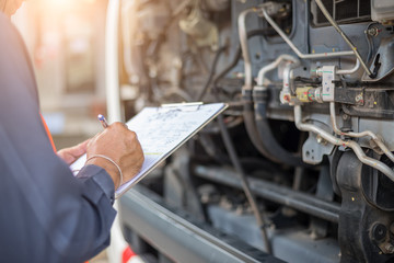 Preforming a pre-trip inspection on a truck,Concept preventive maintenance truck checklist,Truck driver holding clipboard with checking of truck,spot focus.
