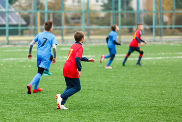 Fototapeta premium Boys in red white blue sportswear running on soccer field. Young footballers dribble and kick football ball in game. Training, active lifestyle, sport, children activity concept