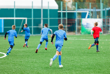 Football training for kids. Boys in blue red sportswear on soccer field. Young footballers dribble and kick ball in game. Training, active lifestyle, sport, children activity concept 