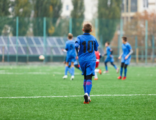 Fototapeta premium Boys in red white blue sportswear running on soccer field. Young footballers dribble and kick football ball in game. Training, active lifestyle, sport, children activity concept