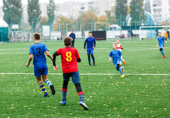 Obraz premium Boys in red white blue sportswear running on soccer field. Young footballers dribble and kick football ball in game. Training, active lifestyle, sport, children activity concept