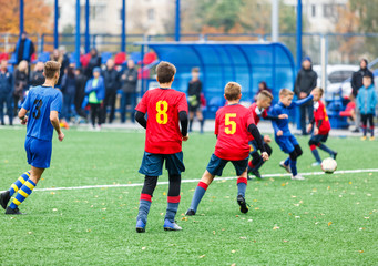 Obraz na płótnie Canvas Boys in red white blue sportswear running on soccer field. Young footballers dribble and kick football ball in game. Training, active lifestyle, sport, children activity concept