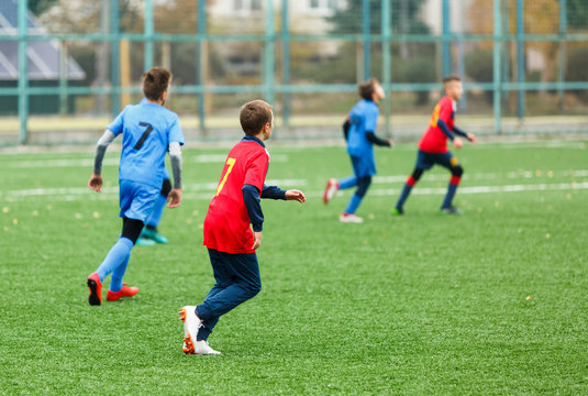 Boys in red white blue sportswear running on soccer field. Young footballers dribble and kick football ball in game. Training, active lifestyle, sport, children activity concept
