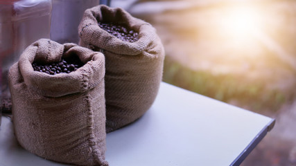 Coffee beans in a sack canvas on wooden table white.