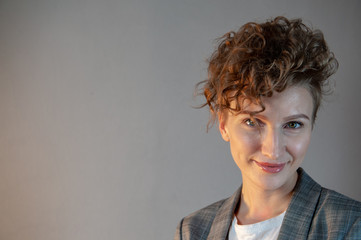 young blonde in gray jacket with short haircut. woman poses for camera, demonstrating natural beauty with beautiful make-up and curled hair. Tender emotions and coquetry