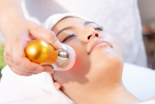 Rejuvenating facial therapy treatment at spa salon clinic. Young beautiful Asian woman getting lifting anti-aging, face massage and skincare by electroporation facial therapy aesthetic cosmetology.