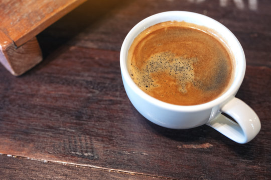 Closeup image of a white cup of hot coffee on vintage wooden table in cafe