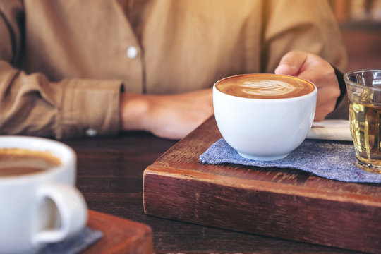 Closeup image of woman's hands holding a cup of hot coffee on wooden table