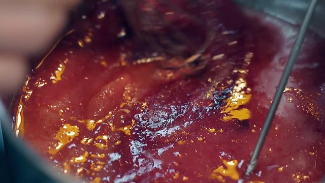 close view confectioner melts sugar with red food pigment in stewpan to prepare caramel using metal whisk
