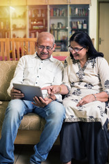Indian/asian Senior couple video chatting on tablet/computer while sitting at couch or in garden at...