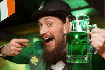 Dark-haired bearded young man in a leprechaun costume celebrating in the pub