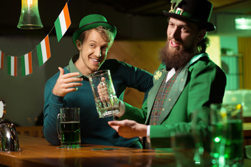 Dark-haired bearded young man in a leprechaun hat showing an empty glass