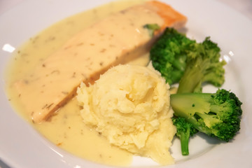 Delicious bake salmon fillet topped with garlic lemon cream sauce serving with mashed potato and boiled broccoli. 