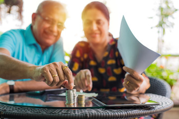 Senior Indian/asian couple arranging/staking coins pile in a row, selective focus