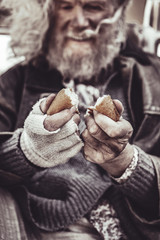 Homeless elderly sitting and sharing sweet bun to two portions.